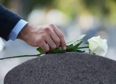 Person placing a rose on top of the grave of a wrongful death victim.