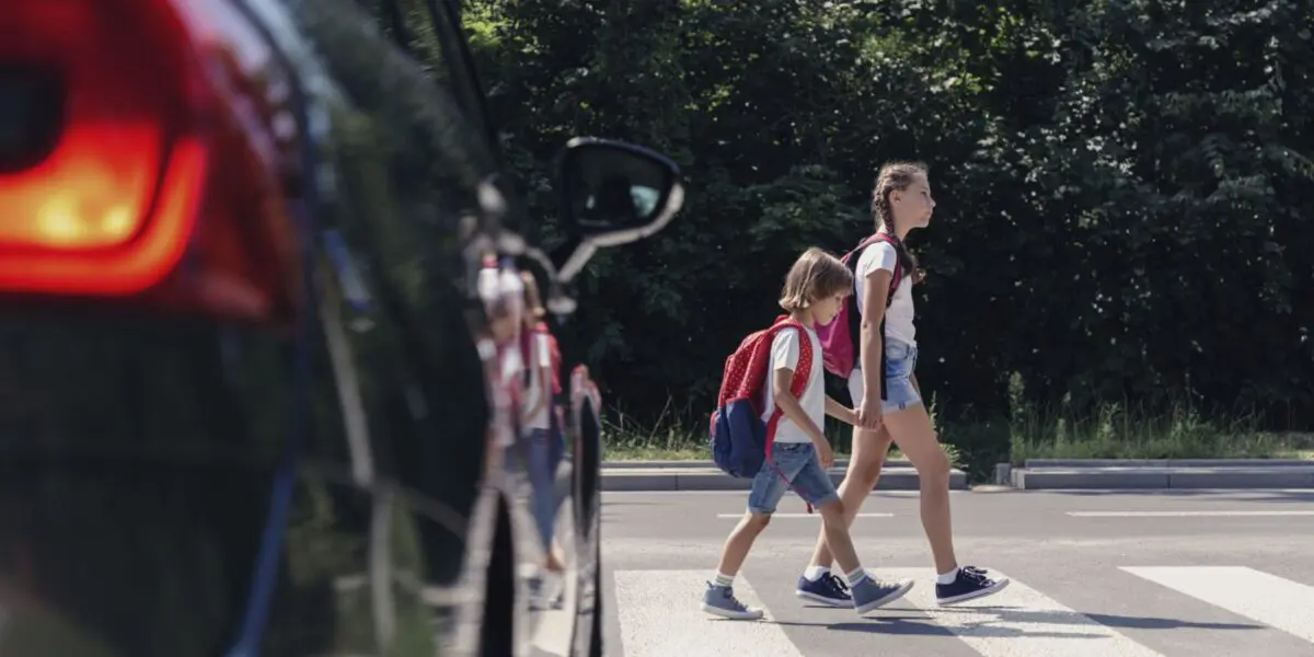 school children crossing the crosswalk in front of black car