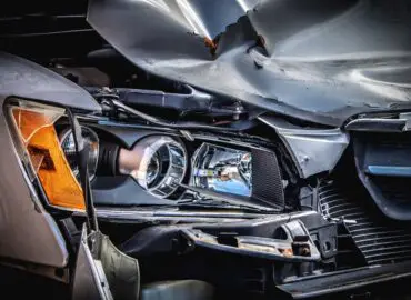 Close Up Of Car Accident Damage to front right of a silver vehicle, smashed in headlight, bumper, grill, and fender.
