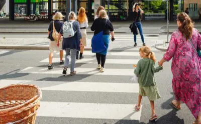child in green holding hands with mother while crossing crosswalk
