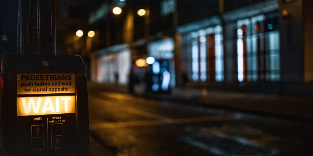 dark roadway with crosswalk sign lighting up "wait"