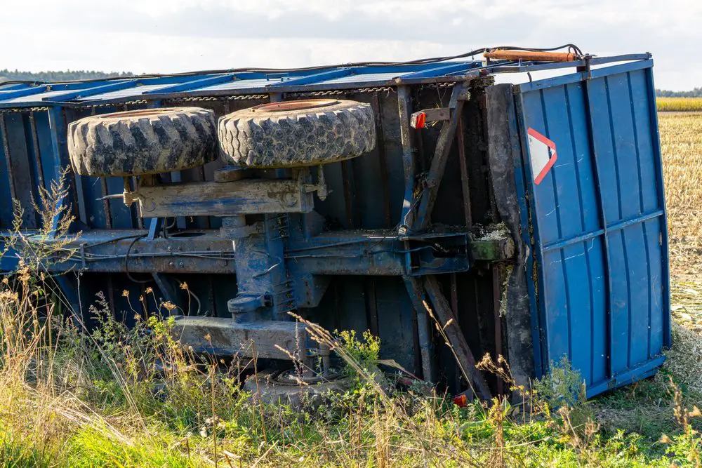 Overturned metal trailer with damage in a crop field after an agricultural accident