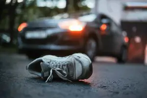 Shoe lying on asphalt after a car accident, with a vehicle in the background