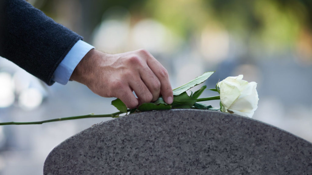 Person placing a rose on top of the grave of a wrongful death victim.