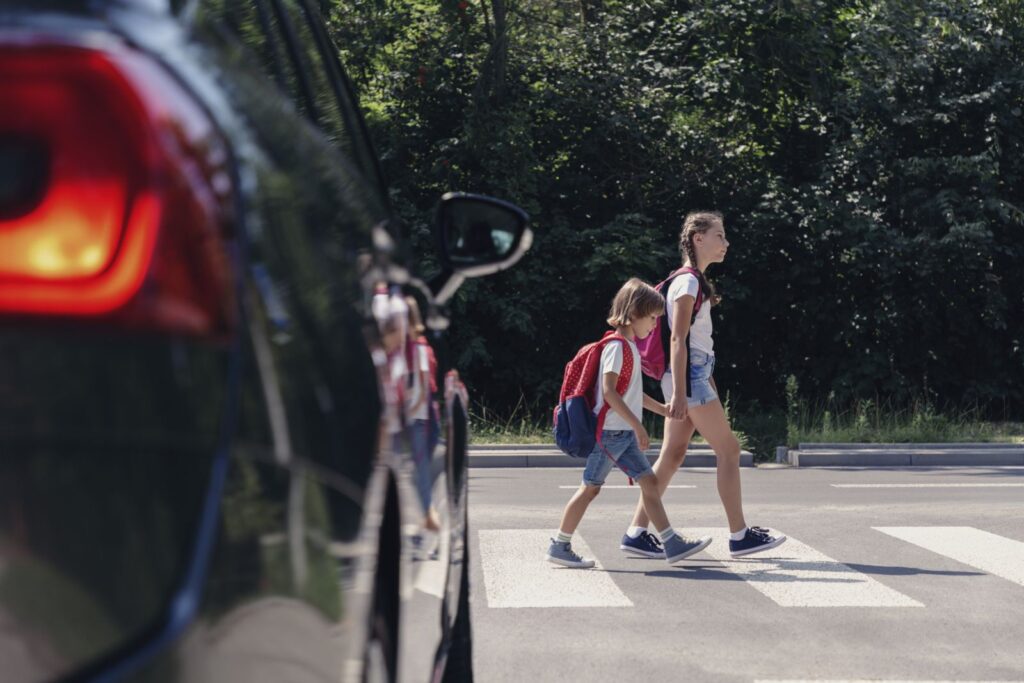 school children crossing the crosswalk in front of black car